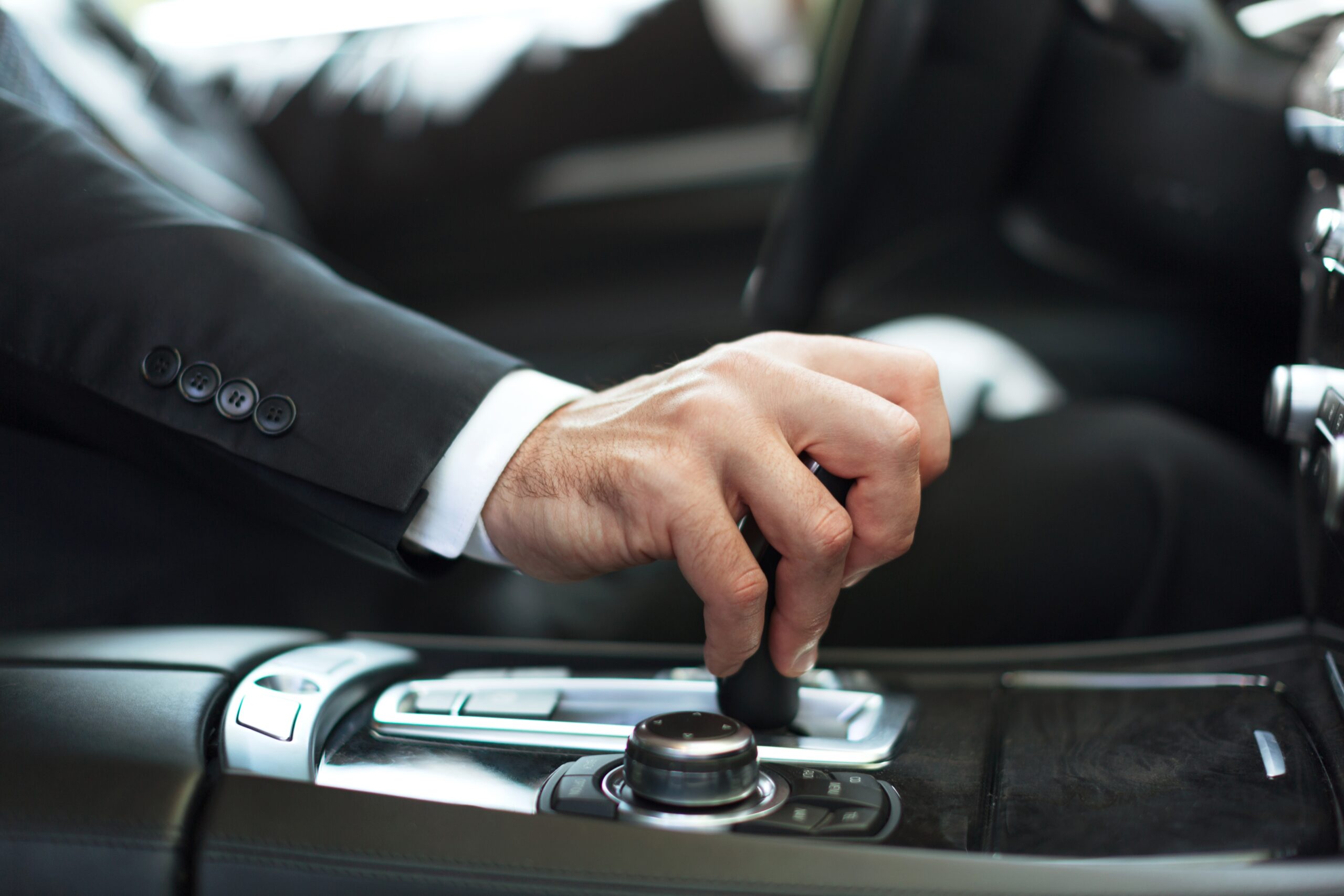 Car. Businessman driving his car on background. Close-up human hand holding gear shift knob